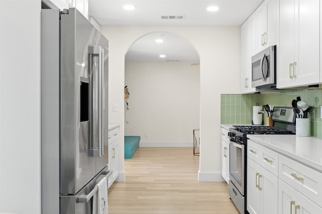 kitchen with white cabinets, appliances with stainless steel finishes, light hardwood / wood-style floors, and tasteful backsplash