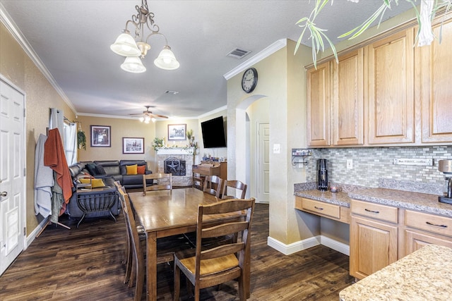 dining space with dark hardwood / wood-style flooring, a stone fireplace, crown molding, and ceiling fan with notable chandelier