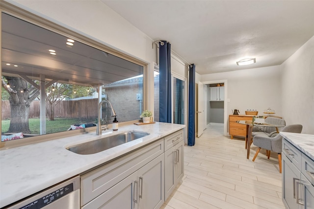 kitchen featuring sink, stainless steel dishwasher, light wood-type flooring, and light stone countertops