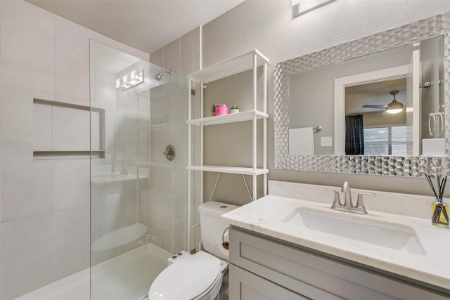 bathroom featuring toilet, a tile shower, vanity, and ceiling fan