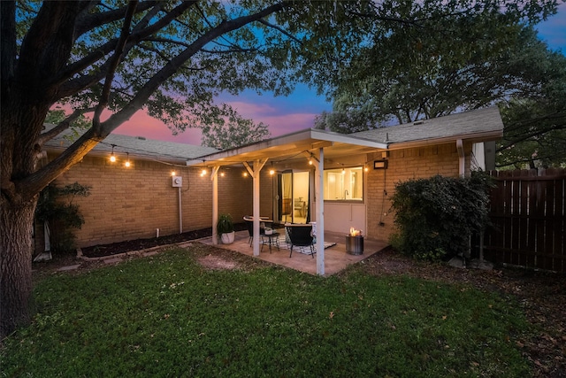 back house at dusk featuring a patio and a lawn