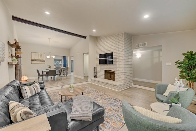 living room featuring light hardwood / wood-style floors, an inviting chandelier, lofted ceiling with beams, and a fireplace