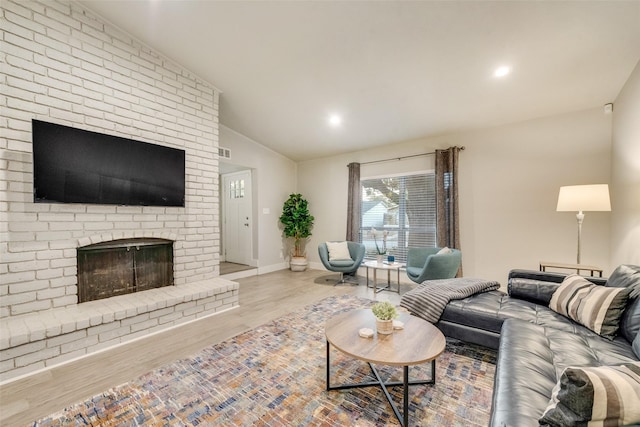 living room featuring lofted ceiling, a brick fireplace, and light hardwood / wood-style floors