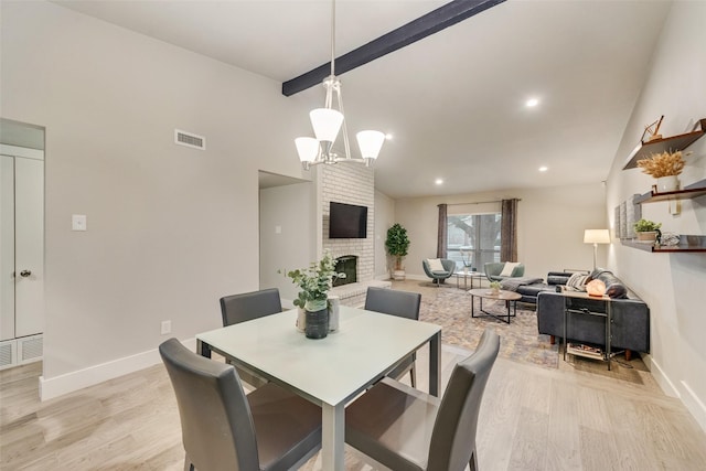 dining space featuring a notable chandelier, light hardwood / wood-style flooring, a brick fireplace, and beam ceiling