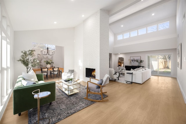 living room featuring light wood-type flooring, a high ceiling, an inviting chandelier, and a fireplace