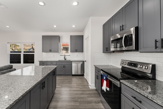 kitchen with stainless steel appliances, gray cabinets, and light stone countertops