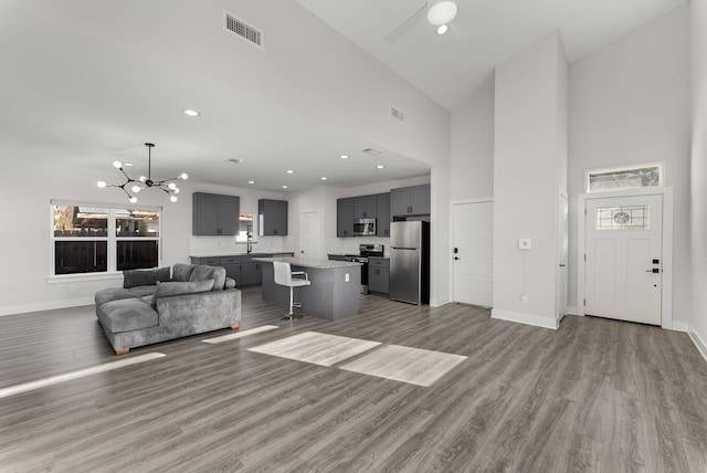 living room featuring ceiling fan with notable chandelier, high vaulted ceiling, sink, and light wood-type flooring