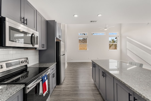 kitchen featuring gray cabinetry, stainless steel appliances, light stone countertops, ceiling fan, and tasteful backsplash