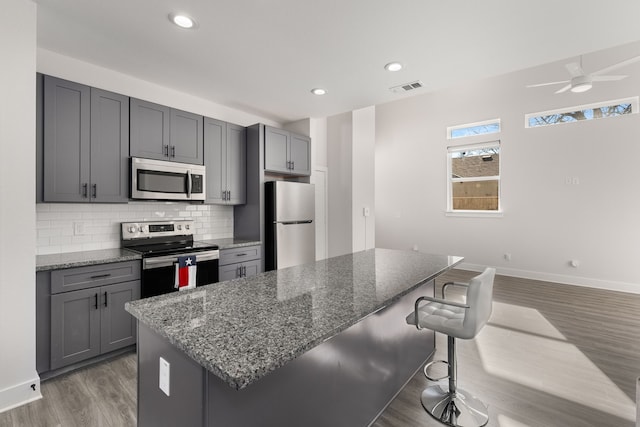 kitchen with stainless steel appliances, dark stone countertops, a breakfast bar, and gray cabinetry