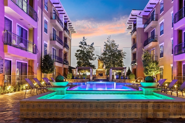 pool at dusk featuring an outdoor fireplace