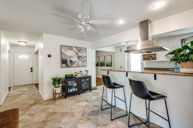 kitchen featuring a breakfast bar area, white cabinets, island range hood, and ceiling fan