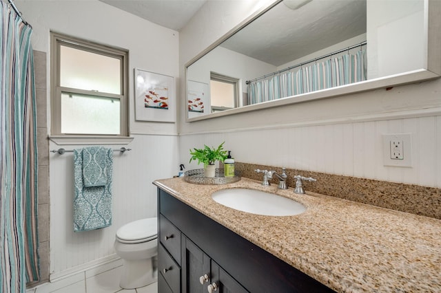 bathroom featuring tile patterned flooring, wooden walls, vanity, and toilet