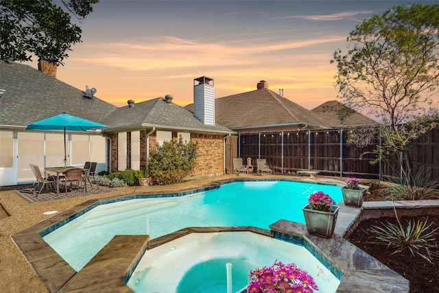 pool at dusk with an in ground hot tub