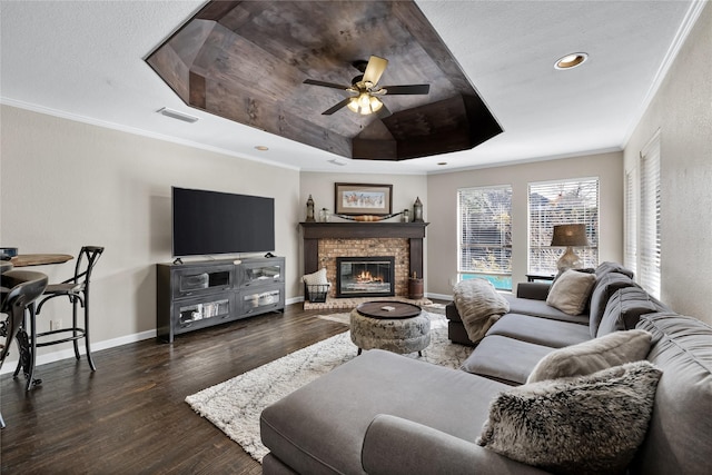 living room with a raised ceiling, ceiling fan, dark hardwood / wood-style flooring, ornamental molding, and a fireplace