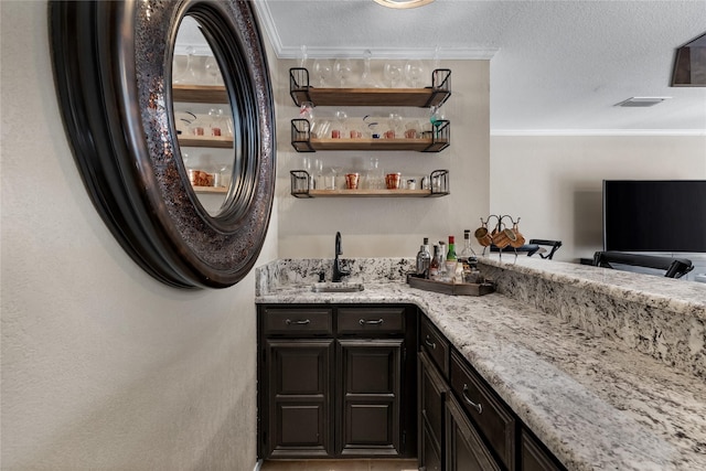 bar featuring sink, ornamental molding, dark brown cabinets, and light stone counters