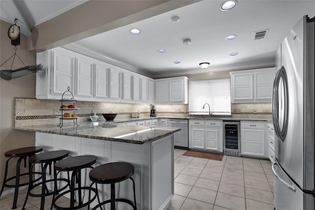 kitchen with white cabinets, kitchen peninsula, beverage cooler, dark stone counters, and appliances with stainless steel finishes