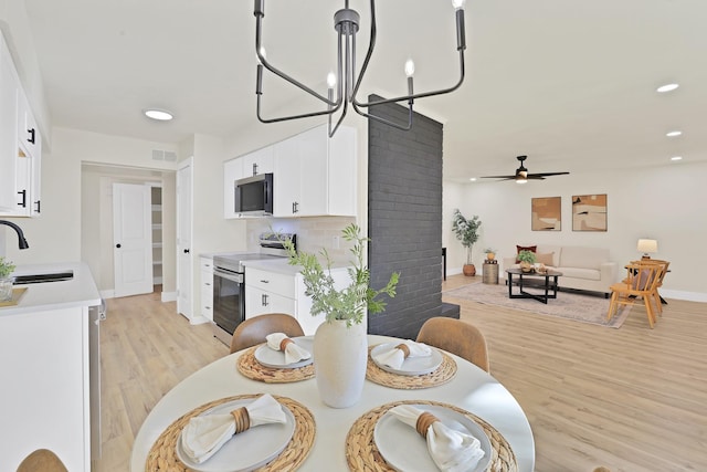 dining space featuring sink, light hardwood / wood-style floors, and ceiling fan with notable chandelier