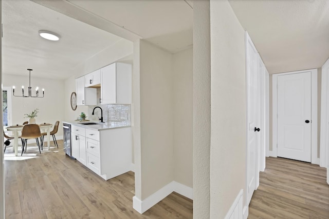 kitchen with sink, white cabinets, an inviting chandelier, light wood-type flooring, and tasteful backsplash