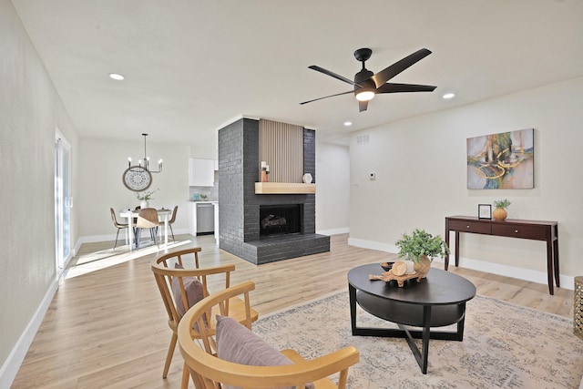 living room featuring ceiling fan with notable chandelier, a fireplace, and light wood-type flooring