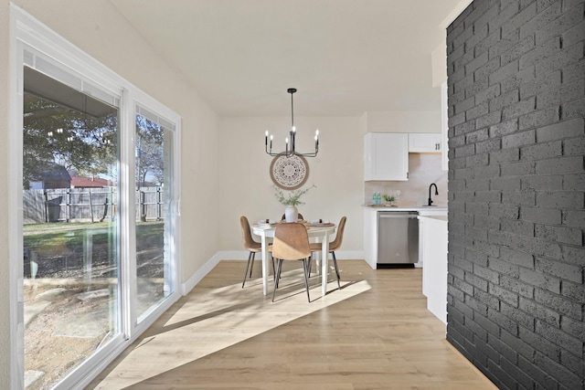 dining room with brick wall, light wood-type flooring, a wealth of natural light, and an inviting chandelier