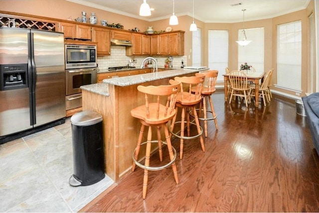 kitchen featuring kitchen peninsula, light stone countertops, pendant lighting, stainless steel appliances, and decorative backsplash