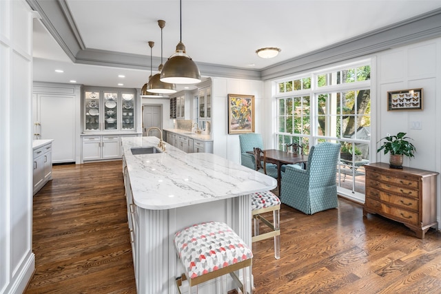 kitchen with an island with sink, ornamental molding, dark wood-type flooring, sink, and decorative light fixtures