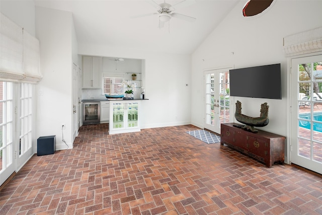 unfurnished living room with high vaulted ceiling, ceiling fan, french doors, and wine cooler