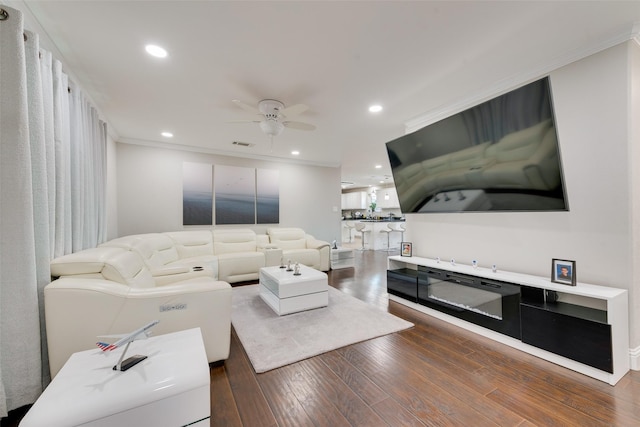 living room with dark wood-type flooring, ceiling fan, and crown molding