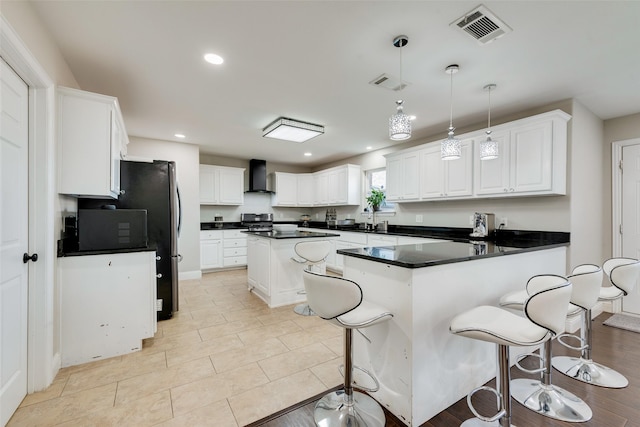 kitchen featuring white cabinets, light tile patterned floors, wall chimney range hood, pendant lighting, and appliances with stainless steel finishes