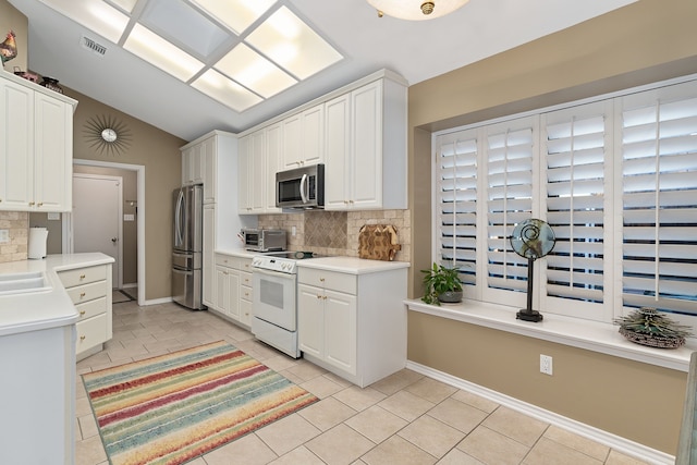 kitchen with appliances with stainless steel finishes, white cabinetry, backsplash, and lofted ceiling