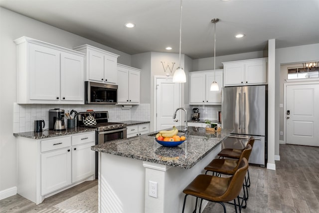 kitchen featuring decorative light fixtures, a kitchen island with sink, white cabinets, appliances with stainless steel finishes, and sink