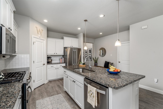 kitchen with sink, stainless steel appliances, tasteful backsplash, an island with sink, and hanging light fixtures