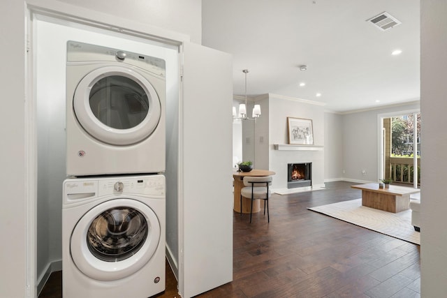 laundry area featuring stacked washer and clothes dryer, a notable chandelier, crown molding, and dark hardwood / wood-style floors