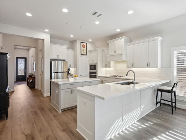 kitchen with kitchen peninsula, stainless steel appliances, decorative backsplash, light wood-type flooring, and white cabinets