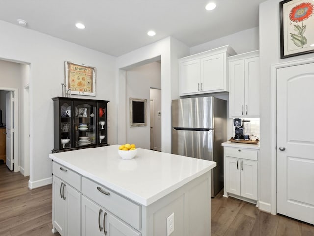 kitchen with hardwood / wood-style floors, stainless steel fridge, a kitchen island, white cabinets, and tasteful backsplash