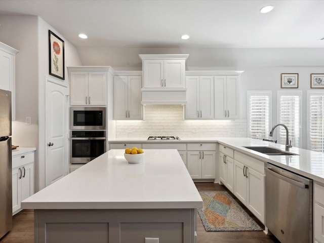 kitchen featuring stainless steel appliances, sink, white cabinets, a center island, and backsplash