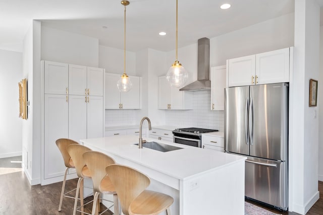 kitchen featuring appliances with stainless steel finishes, an island with sink, white cabinets, wall chimney range hood, and sink