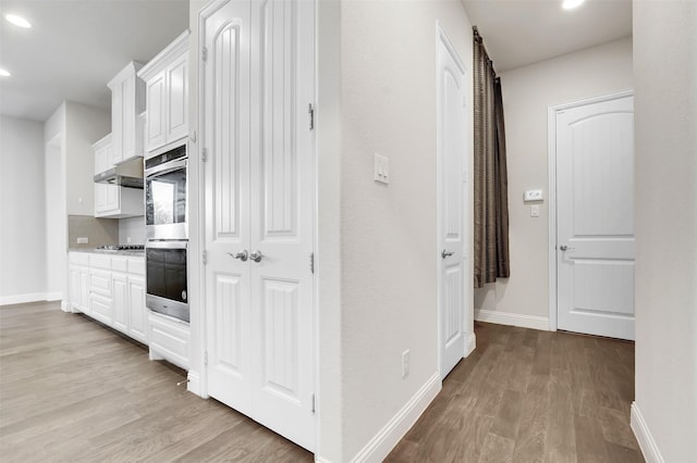 kitchen with light hardwood / wood-style floors, double oven, decorative backsplash, white cabinets, and black gas stovetop