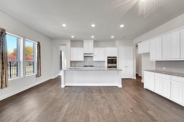 kitchen featuring sink, white cabinetry, light stone counters, and an island with sink