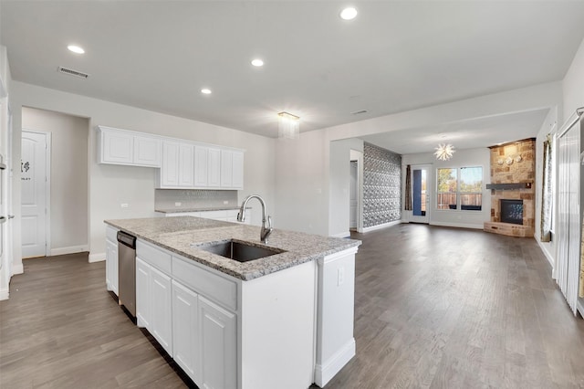 kitchen with a kitchen island with sink, light stone counters, a fireplace, sink, and white cabinetry