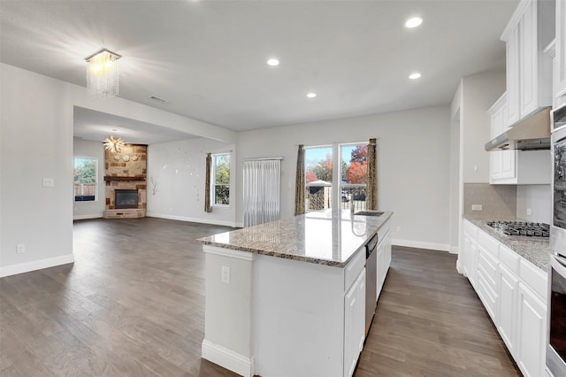 kitchen featuring white cabinets, a stone fireplace, light stone countertops, and a center island with sink