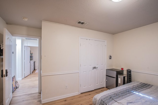 bedroom with a closet, light hardwood / wood-style floors, and stainless steel fridge