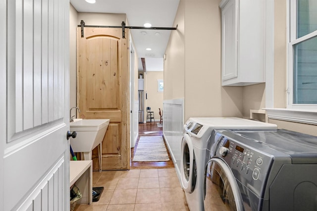 washroom featuring washing machine and dryer, a barn door, light tile patterned floors, and cabinets