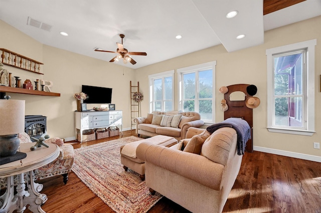 living room with dark wood-type flooring, ceiling fan, and a wood stove