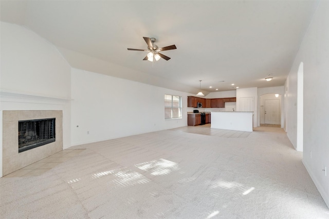 unfurnished living room with a tiled fireplace, ceiling fan, and light colored carpet