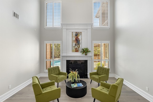 living area with a towering ceiling, wood-type flooring, and a premium fireplace