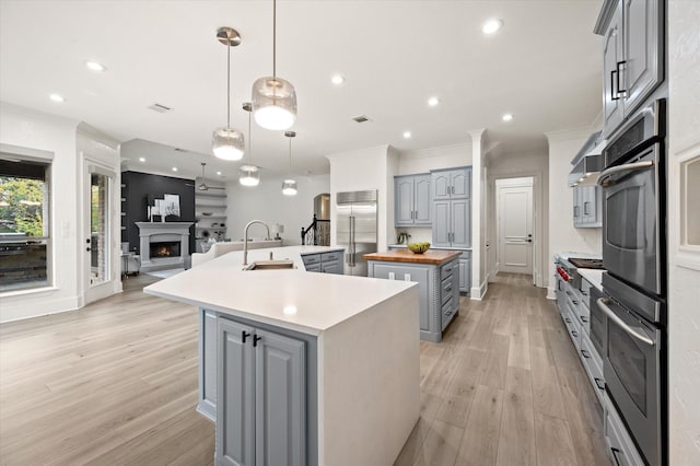 kitchen with decorative light fixtures, sink, an island with sink, butcher block counters, and stainless steel appliances