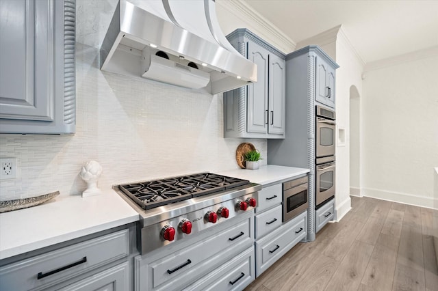 kitchen with appliances with stainless steel finishes, light hardwood / wood-style floors, backsplash, ornamental molding, and range hood