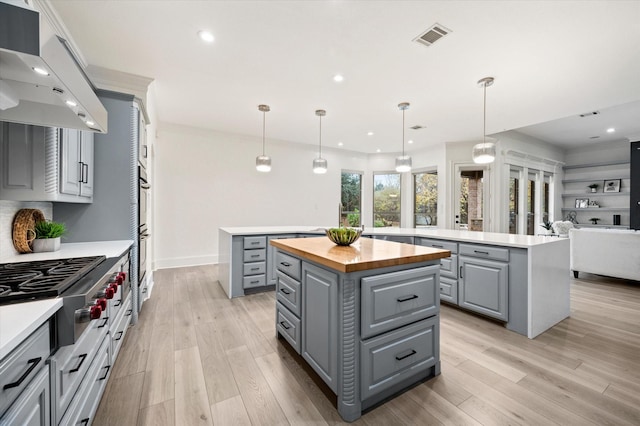 kitchen with a center island, premium range hood, hanging light fixtures, gray cabinetry, and butcher block countertops