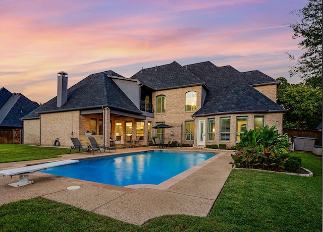 pool at dusk featuring a diving board, a patio area, and a lawn